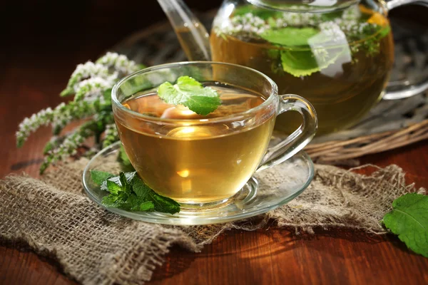 Tazza e teiera di tisana con fiori di menta freschi sul tavolo di legno — Foto Stock