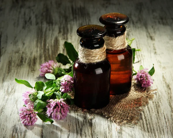 Medicine bottles with clover flowers on wooden table — Stock Photo, Image