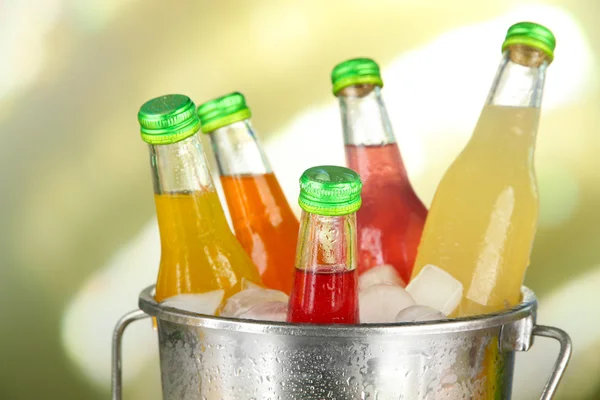 Botellas con sabrosas bebidas en cubo con cubitos de hielo, en un fondo brillante —  Fotos de Stock