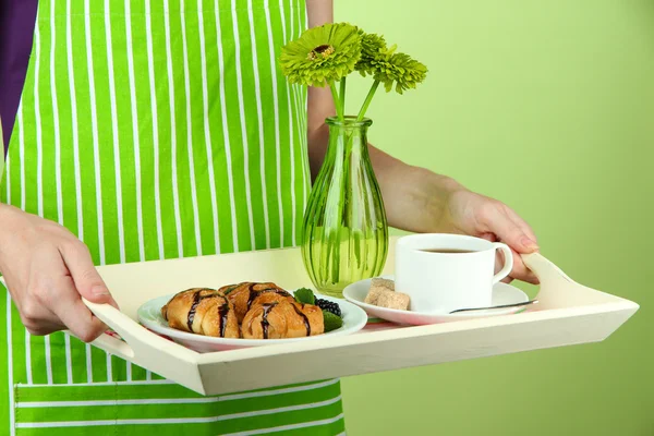 Mulher em avental verde segurando bandeja de madeira com café da manhã, em fundo de cor — Fotografia de Stock