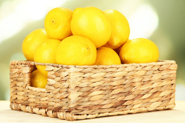 Ripe lemons in wicker basket on table on bright background