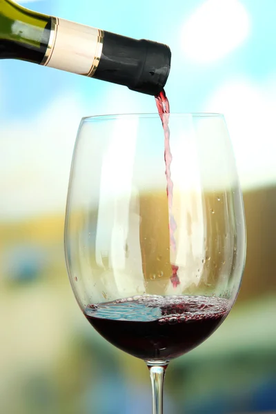 Vino tinto que se vierte en copa de vino, sobre fondo brillante — Foto de Stock
