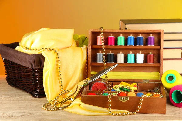 Kit de costura en caja de madera con libros y mesa de tela sobre fondo brillante — Foto de Stock