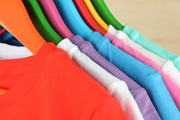 Different shirts on colorful hangers on light background — Stock Photo, Image