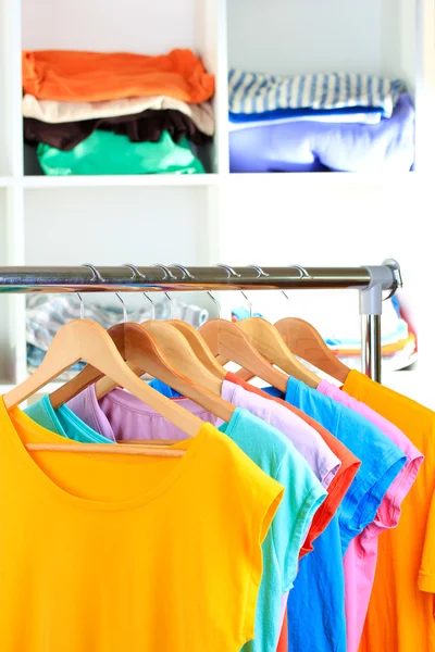 Verscheidenheid van casual t-shirts op houten hangers op planken achtergrond — Stockfoto