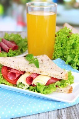 Lezzetli sandviç salam sosis ve ahşap masa arka plan üzerinde renkli peçete üzerinde sebze ve meyve suyu ile kompozisyon