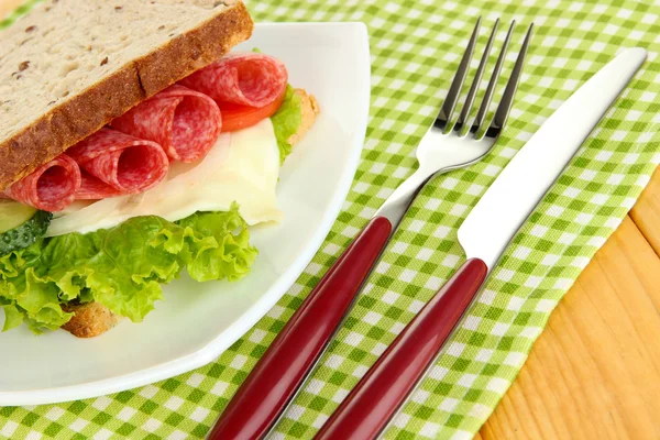 Sanduíche saboroso com salsicha de salame e legumes na placa branca, no fundo de madeira — Fotografia de Stock