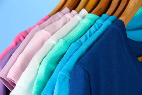 Verschiedene lässige Hemden auf Holzbügeln, auf blauem Hintergrund — Stockfoto