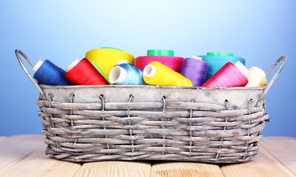 Bright threads in basket on wooden table on blue background — Stock Photo, Image