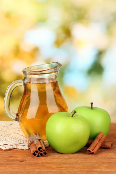 Full jug of apple juice and apple on wooden table on bright background — Stock Photo, Image