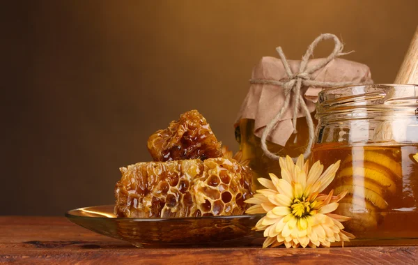 Due vasetti di miele, favi e drizzler in legno su tavola su fondo giallo — Foto Stock