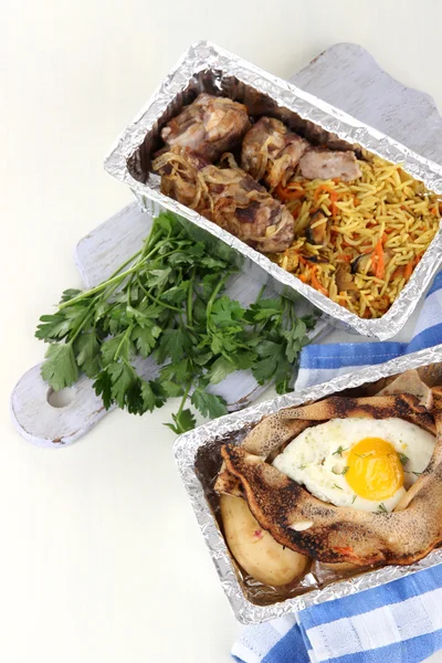 Food in boxes of foil on napkin on wooden board isolated in white