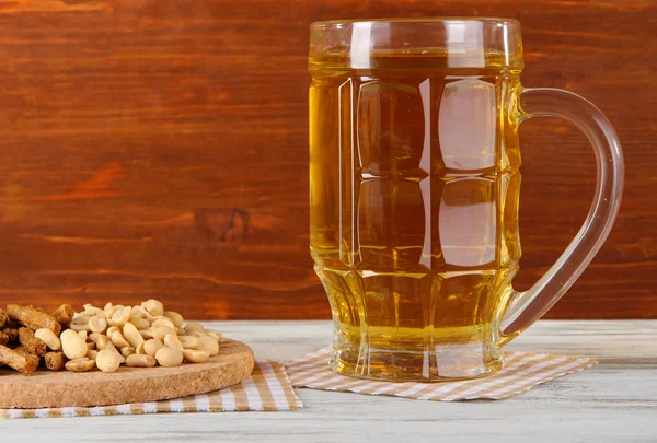 Beer in glass crunches, and nuts on napkin on table on wooden background — Stock Photo, Image