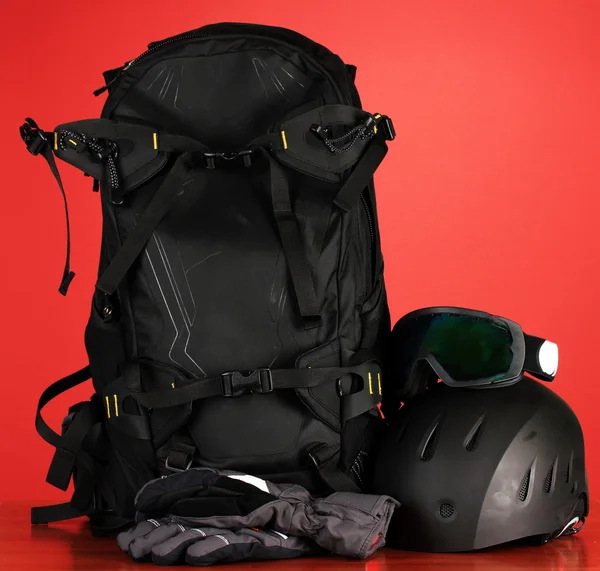 Wintersportbrille, Helm und Handschuhe, Rucksack, auf rotem Hintergrund — Stockfoto