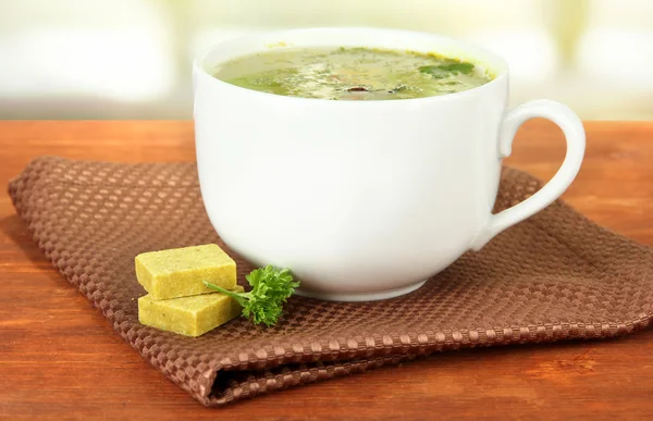 Kopje soep met bouillonblokjes op houten tafel — Stockfoto