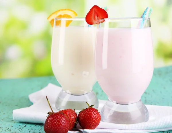 Deliziosi frullati di latte con arancia e fragole su tavolo di legno su sfondo naturale — Foto Stock