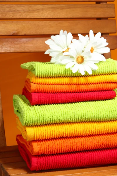 Handdukar och blommor på trä stol på orange bakgrund — Stockfoto