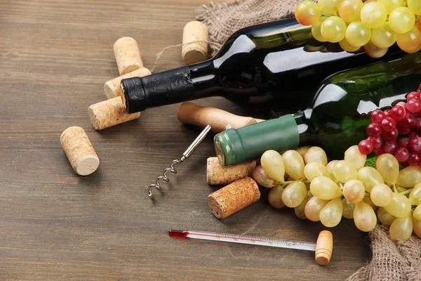 Garrafas de vinho, uvas e rolhas sobre fundo de madeira — Fotografia de Stock