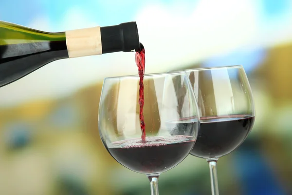 Red wine being poured into wine glass, on bright background — Stock Photo, Image