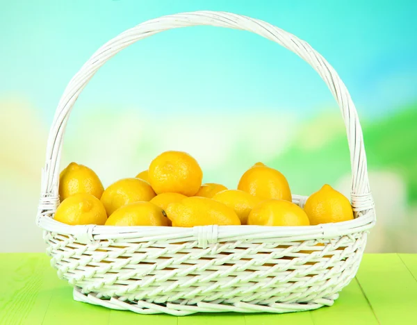 Limones maduros en canasta de mimbre sobre mesa sobre fondo brillante — Foto de Stock