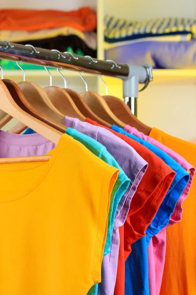Variety of casual t-shirts on wooden hangers on shelves background — Stock Photo, Image