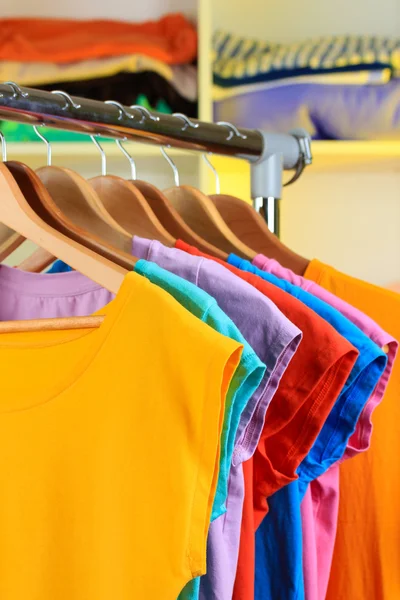 Variedade de camisetas casuais em cabides de madeira em prateleiras fundo — Fotografia de Stock