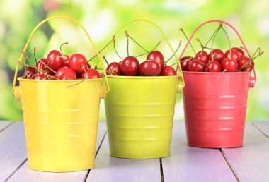 parlak zemin üzerine ahşap masa üzerinde renkli kova içinde kiraz meyveleri
