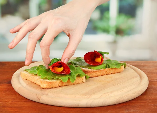 Processo de preparar rolos de salame no pão assado, no fundo brilhante: a mão feminina põe o rolo de salame com o pedaço de páprica no pão assado — Fotografia de Stock