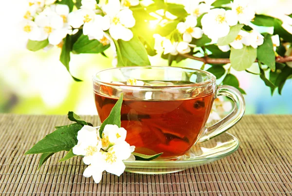 Cup of tea with jasmine, on bamboo mat, on bright background — Stock Photo, Image