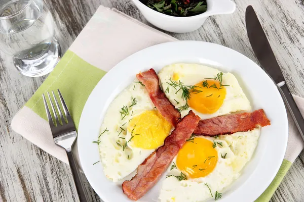 Scrambled eggs and bacon on plate on napkin on wooden table — Stock Photo, Image