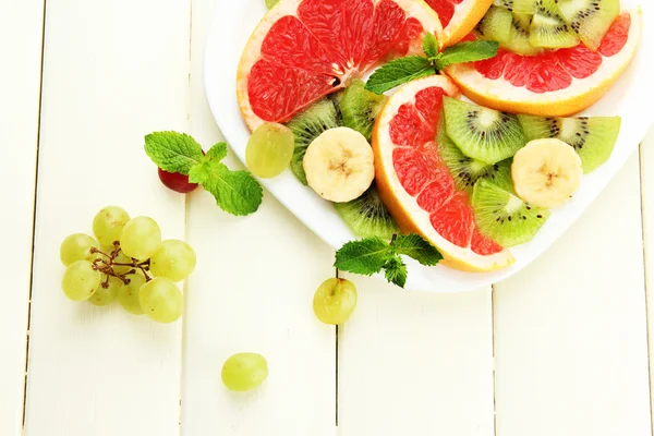 Surtido de frutas en rodajas en plato, sobre mesa de madera blanca — Foto de Stock