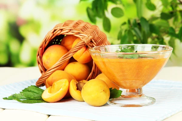 Confiture d'abricots dans un bol en verre et abricots frais, sur table en bois, sur fond lumineux — Photo