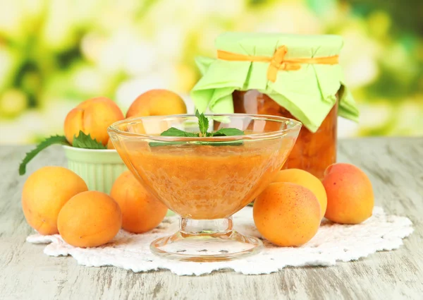 Apricot jam in glass jar and fresh apricots, on wooden table, on bright background — Stock Photo, Image