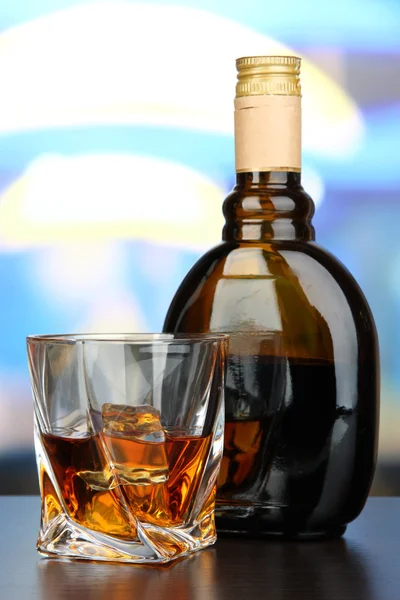 Glass of liquor with bottle, on dark background