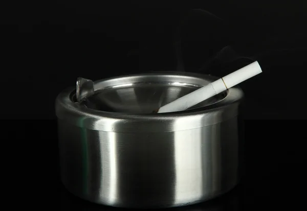 Cenicero de metal y cigarrillo sobre fondo negro — Foto de Stock
