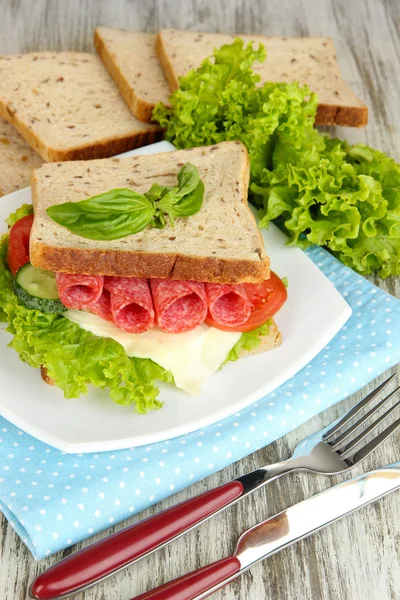 Komposition med fruktjuice och god smörgås med salami korv och grönsaker på färg Servett, på träbord bakgrund — Stockfoto