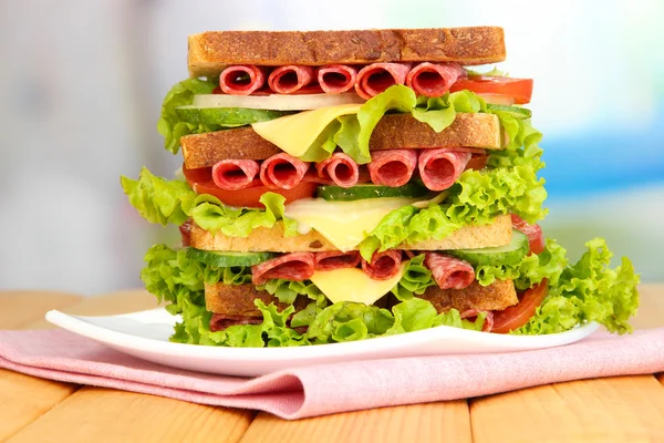 Huge sandwich on wooden table, on bright background — Stock Photo, Image