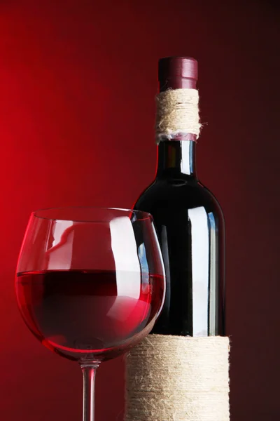 Copo de vinho com garrafa no fundo vermelho brilhante — Fotografia de Stock