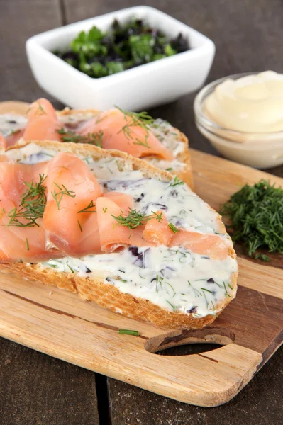 Sandwiches de pescado sobre tabla de cortar sobre mesa de madera — Foto de Stock