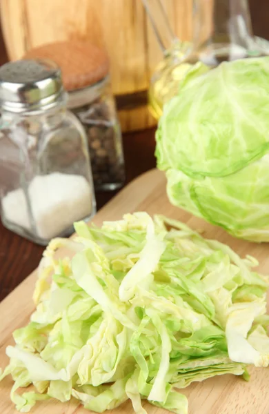 Green cabbage, oil, spices on cutting board, on wooden background