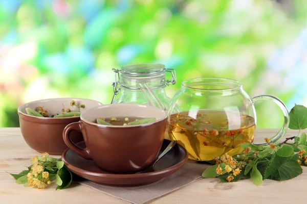 Kettle and cup of tea with linden on wooden table on nature background — Stock Photo, Image