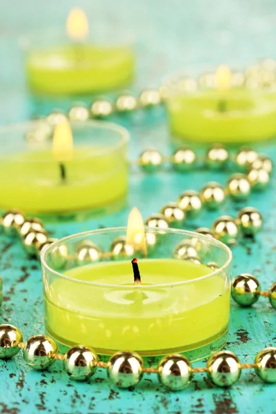 Lighted candles with beads on green background — Stock Photo, Image