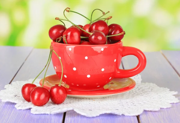 Cherry berries in cup on wooden table on bright background — Stock Photo, Image