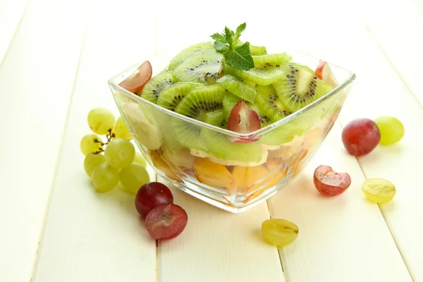 Smakelijke fruitsalade in glazen kom, op witte houten tafel — Stockfoto