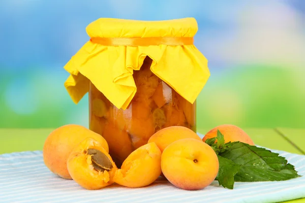 Marmellata di albicocche in vaso di vetro e albicocche fresche, su tavolo di legno, su sfondo brillante — Foto Stock