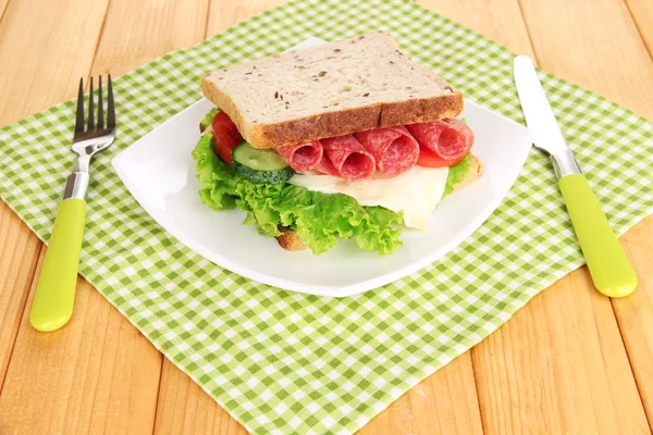 Sanduíche saboroso com salsicha de salame e legumes na placa branca, no fundo de madeira — Fotografia de Stock