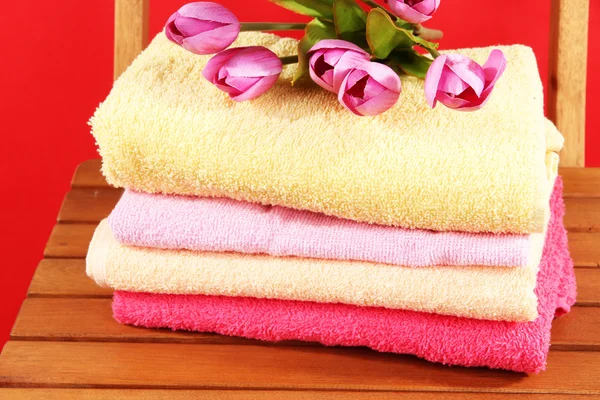 Towels and flowers on wooden chair on red background — Stock Photo, Image