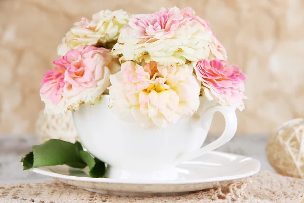 Розы в чашке на салфетках на деревянном столе на бежевом фоне — стоковое фото
