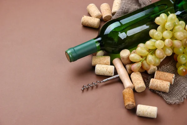 Bottle of wine, grapes and corks on brown background — Stock Photo, Image