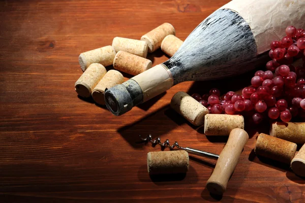 Stará láhev vína, vinných hroznů a zátky na dřevěné pozadí — Stock fotografie